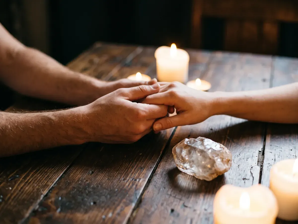Dos manos entrelazadas sobre una mesa de madera con velas encendidas